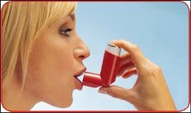 Profilo di una donna bionda che utilizza un inalatore spray rosso tenendolo con la mano davanti alla bocca aperta su sfondo azzurro