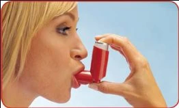 Profilo di una donna bionda che utilizza un inalatore spray rosso tenendolo con la mano destra vicino alle labbra aperte su sfondo azzurro