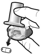 A hand pressing down a medical device to release a capsule, which falls downward as indicated by a curved arrow