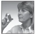 A woman with light-colored hair holds up an asthma inhaler in front of her face, looking at it closely