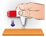 A hand holding a white and red medical device pressing it downward onto a wooden surface with a blue arrow pointing downward