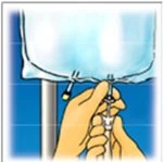 Two hands holding and manipulating the bottom part of a medical infusion bag suspended from a vertical stand against a blue background