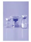 Tre flaconcini di vetro trasparente con tappi metallici disposti su una superficie riflettente con sfondo celeste