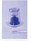 Flacone di vetro trasparente con tappo e contenuto liquido di colore blu intenso su sfondo lilla