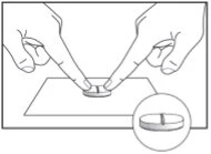 Two fingers pressing on a round tablet placed on a flat surface, with a magnified view showing the central dividing line