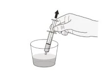 A hand holding a syringe with the needle pointing downward while drawing liquid from a transparent glass with an arrow pointing towards it