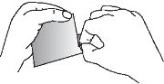 Two hands carefully holding and opening a small pouch or square wrapper made of opaque material to remove its contents