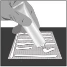 Una mano preme un tubetto di crema per applicare una striscia di prodotto bianco su una superficie a griglia quadrata