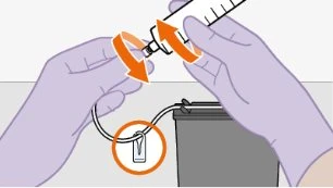 Due mani guantate ruotano una siringa su un dispositivo medico collegato tramite un tubicino bianco con un cerchio arancione in evidenza