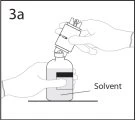 A hand holds an inverted vial above a vial containing solvent to proceed with drug reconstitution