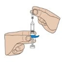 Two hands holding a transparent syringe with liquid and a blue cap while preparing the
