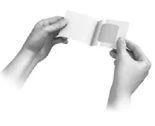 Two hands hold and open a small white rectangular pouch or sachet to remove its contents