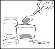 A hand uses a spoon to scoop gray powder from an open container next to a jar, a lid, and a sachet