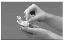 Two hands hold and manipulate a white medical device with a small circular cap or component on a neutral gray background
