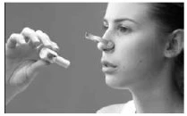 One hand holds a nasal spray near a woman's nose, ready to insert it