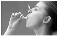 Profile of a woman using an oral inhaler, holding it with her hand near her mouth for administration