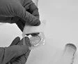 Hands wearing grey gloves carefully opening a transparent blister pack containing a round tablet on a light background
