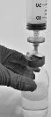 A gloved hand holding a glass vial while a