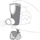 A hand holding an inhaler with the cap removed while a spray cloud is being emitted from it