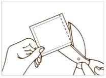 A hand holding a small square pouch while a pair of scissors cuts along the dotted side edge