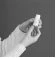 A gloved hand holds vertically a small glass vial with a white cap against a uniform dark background