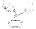 Two hands pouring liquid from a bottle into a spoon held above an empty bowl