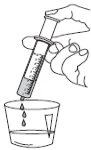 A hand holding a tilted syringe while drawing or pouring liquid into a small transparent cup, with drops falling downward