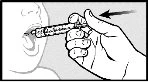 A hand holds a needle-free syringe to administer medication directly into the open mouth of a newborn, with a directional arrow