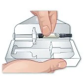A hand holding a horizontal syringe above an open white container with compartments for medication storage