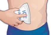 A hand holding a white ice pack with blue text, applying it to the abdomen