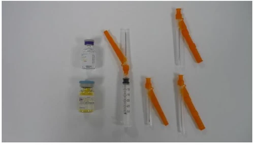 Two glass vials with blue and yellow caps, a syringe with a needle, and three medical devices with orange protective covers on a white background