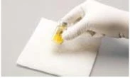 A gloved hand holds a small glass vial containing a yellow liquid above a white gauze pad on a gray background