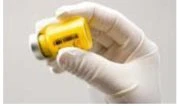 Una mano inguantata di bianco tiene tra le dita una fiala di vetro contenente un liquido giallo brillante su sfondo neutro