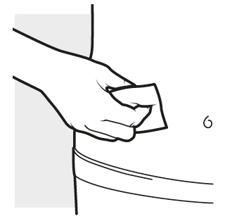 Una mano sostiene un pequeño objeto rectangular blanco sobre una superficie curva clara con el número 6 al lado
