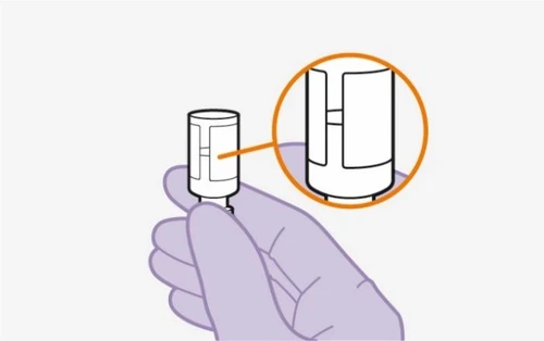Una mano enguantada sostiene un dispositivo médico blanco con un aumento circular que muestra el detalle de la parte superior del