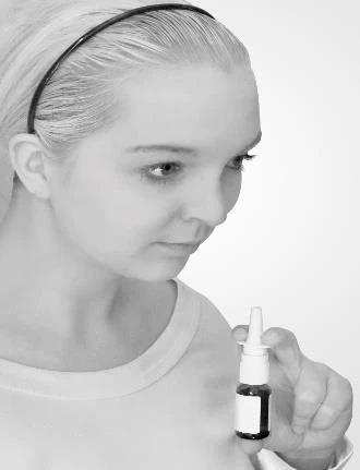 Perfil de una joven mujer rubia que observa atentamente un pequeño frasco de medicamento con gotero que sostiene en la mano