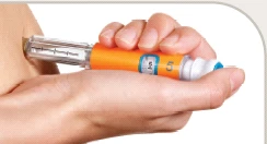 A hand holding an orange and white injection pen while the letter 'l'