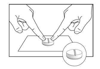 Two hands with index fingers pressing down on a circular tablet split in half placed on a flat surface, with a close-up detail of the pill