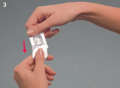 Dos manos abren cuidadosamente una pequeña bolsita de aluminio blanco siguiendo la dirección indicada por una flecha roja vertical