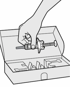 A hand holding a syringe with needle above an open cardboard box with internal compartments for drug containment