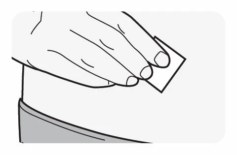 A hand holds a small rectangular patch above the skin of the abdominal or waist area for the