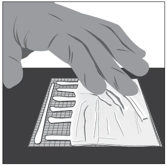 A hand holding and opening a sheet of transparent plastic with an underlying grid to remove a flat, rectangular medical device
