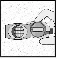 A hand holds an open medical device showing a circular chamber with a grid and an inner compartment containing a capsule inside the