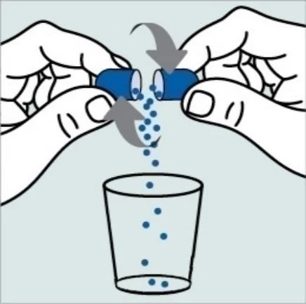 Two hands opening a blue capsule, causing its granular contents to fall out