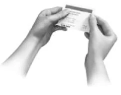 Two hands hold and open a small rectangular leaflet with text and tables against a white background