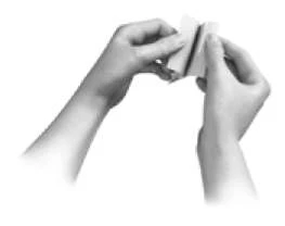 Two hands hold and fold a small white sheet of paper or thin medical device to prepare it