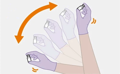 Gloved hands rotating a medical vial following an orange curved arrow indicating rotational movement of the vial