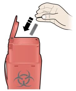 Una mano inserta una aguja usada en un recipiente rojo para residuos biológicos marcado con el símbolo de riesgo biológico