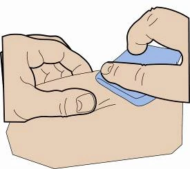 Dos manos sostienen y presionan una pequeña tira rectangular azul sobre una superficie plana y clara para aplicar un dispositivo médico
