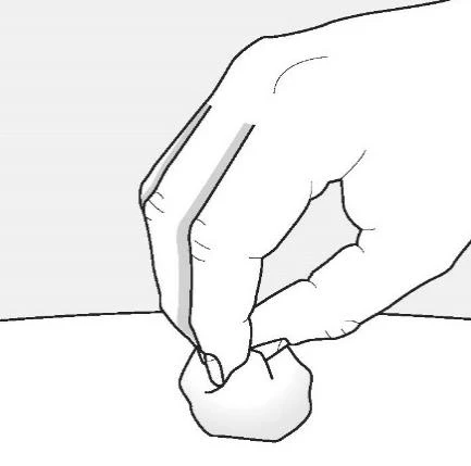 A hand holds between thumb and index finger a small, round white object above a flat surface